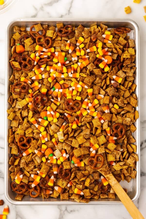 Halloween snack mix with candy corn is spread out on a baking sheet.