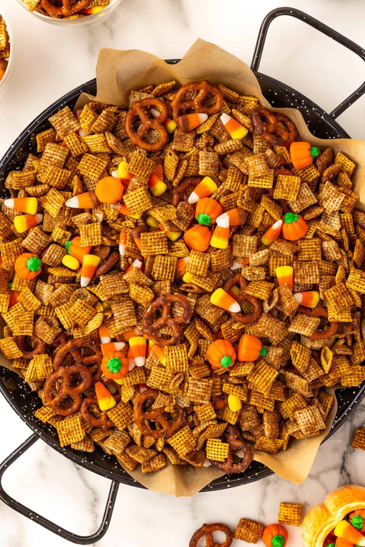 A large black bowl lined with parchment paper is filled with pumpkin spice snack mix.