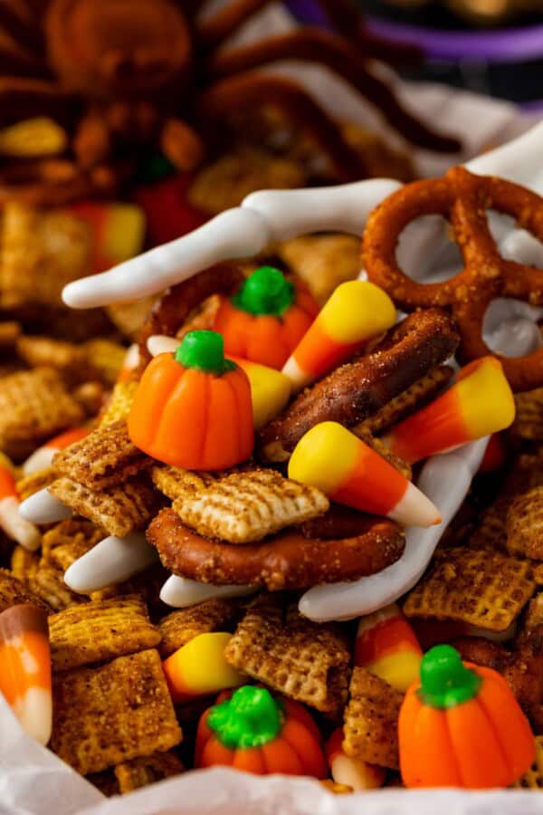 A skeleton hand is holding a portion of pumpkin spice halloween chex mix recipe.