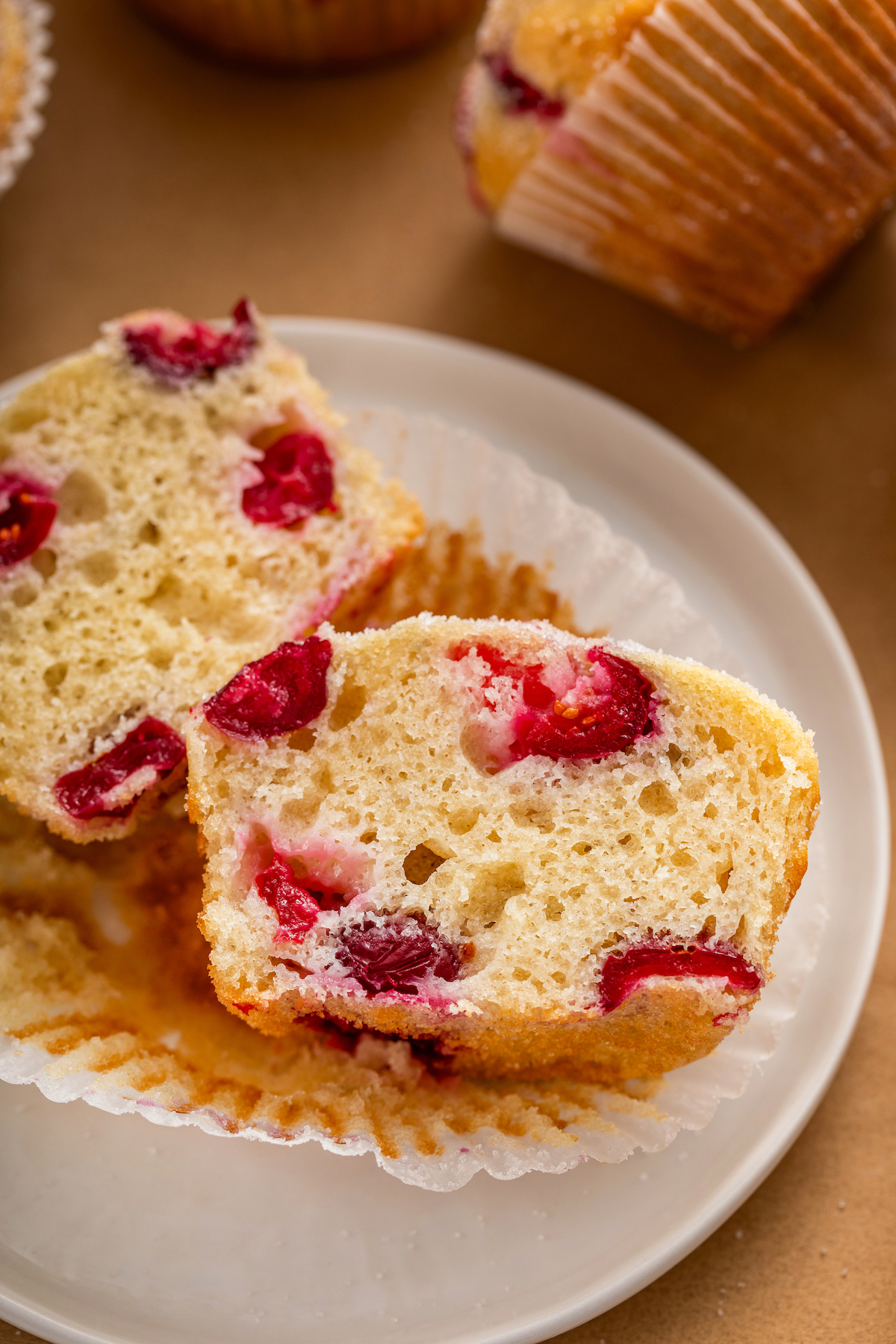 Fresh cranberry muffin sliced in half on a plate with a muffin liner.