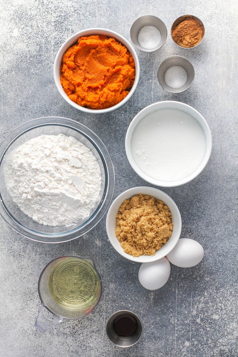 Ingredients for pumpkin muffins in bowls on a gray background.