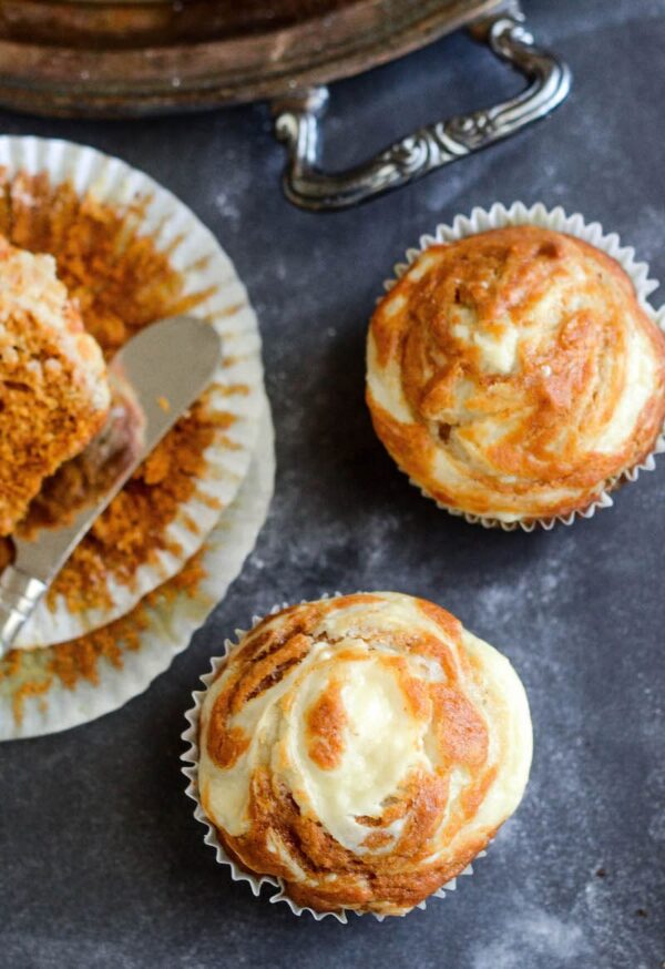 Close up photo of pumpkin cream cheese swirl muffins with one cut in half to see the texture inside. 