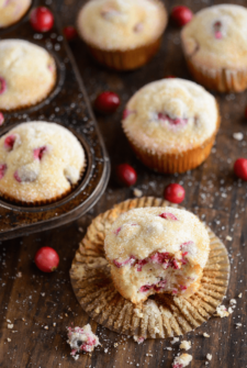 Vanilla Cranberry Sugar Muffins - one with a bite taken out of it - on a dark wooden board