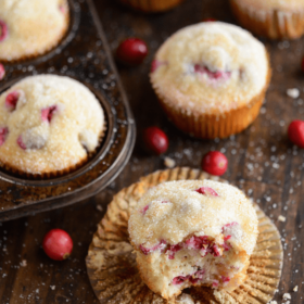 Vanilla Cranberry Sugar Muffins - one with a bite taken out of it - on a dark wooden board