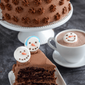 Slice of Hot Chocolate Dream Cake with Snowmen marshmallows and a cup of hot chocolate