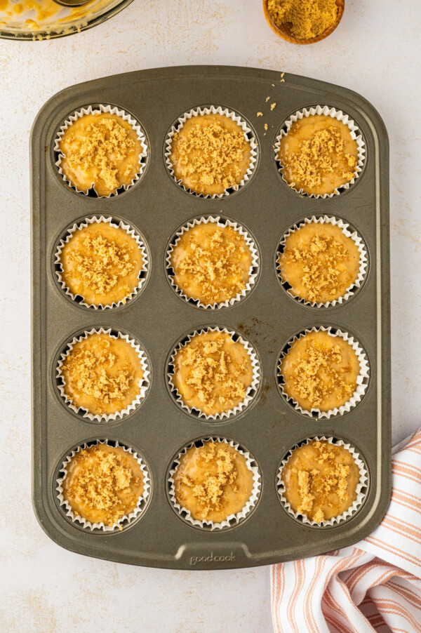 Paper liners in a muffin tin filled with batter and topped with brown sugar.