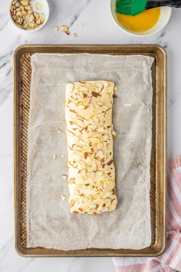 An unbaked braided pastry topped with sliced almonds.