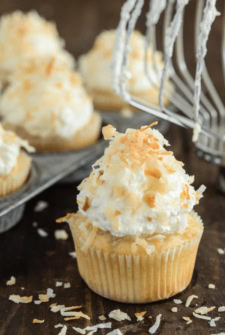 Triple Coconut Poke Cupcakes piled high with whipped cream and shredded coconut