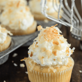 Triple Coconut Poke Cupcakes piled high with whipped cream and shredded coconut
