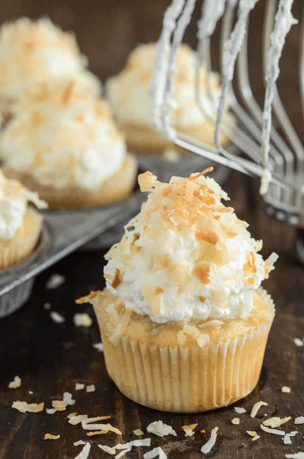 Triple Coconut Poke Cupcakes piled high with whipped cream and shredded coconut