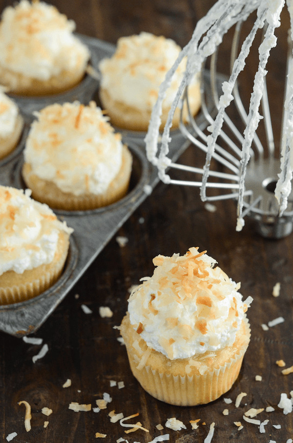 Triple Coconut Poke Cupcakes piled high with whipped cream and shredded coconut