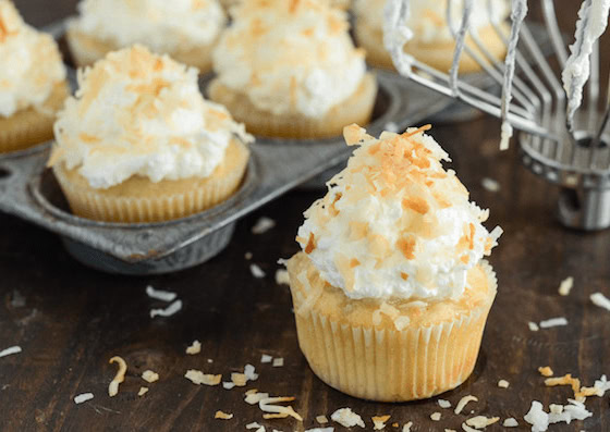 Triple Coconut Poke Cupcakes piled high with whipped cream and shredded coconut