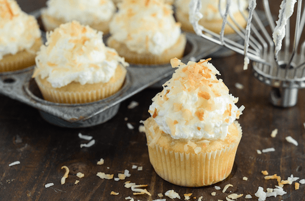 Triple Coconut Poke Cupcakes piled high with whipped cream and shredded coconut