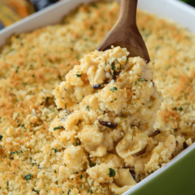 Baked Cauliflower Mac & Cheese in a green casserole with a wooden spoon scooping out of dish