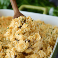 Baked Cauliflower Mac & Cheese in a green casserole with a wooden spoon scooping out of dish