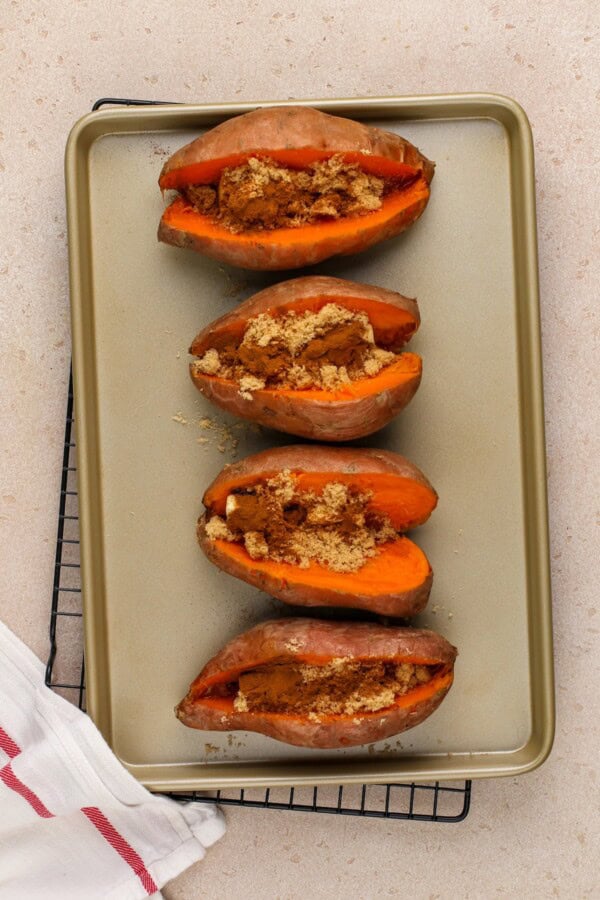 Brown sugar is inside of sliced sweet potatoes on a baking sheet.