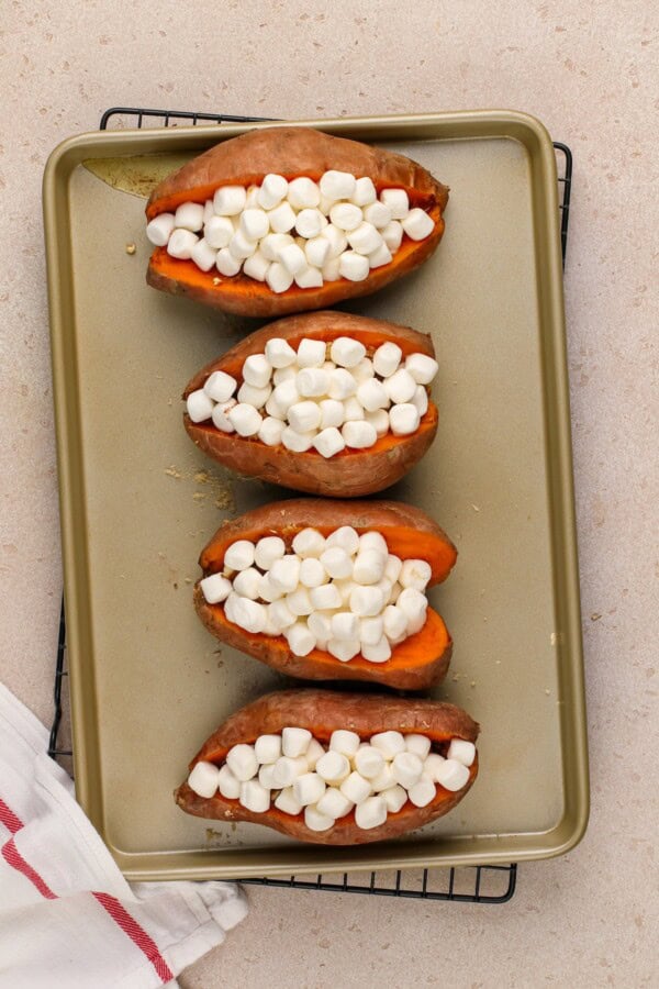 Uncooked marshmallow stuffed sweet potatoes on a baking sheet.