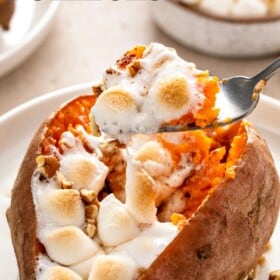 A fork is lifting a bite of sweet potatoes and marshmallows from a plate.