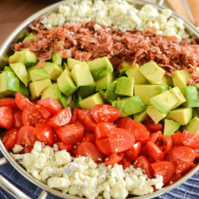 Copycat Maggianos Chopped Salad - blue cheese, tomatoes, avocados, bacon in a silver serving dish on a blue and white cloth