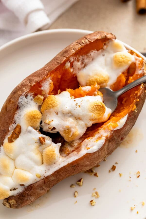 A fork is lifting a bite of gooey marshmallows and sweet potatoes from the plate.