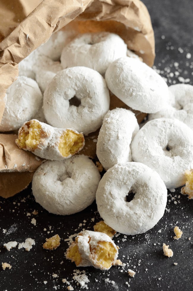 A Paper Bag Full of Mini Powdered Donuts on a Dark Surface