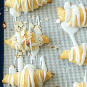 Almond Stuffed Crescent Rolls Lined up on a Baking Sheet with Icing Drizzled Over Them