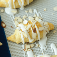 Three Almond Stuffed Crescent Rolls on a Silpat Liner with Toppings Added