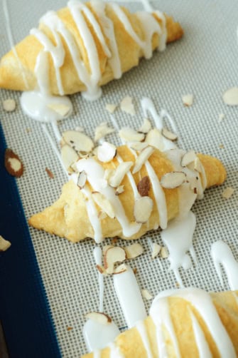 Three Almond Stuffed Crescent Rolls on a Silpat Liner with Toppings Added