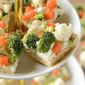 Veggie pizza bars with crescent rolls and ranch spread on a 2-tiered serving tray.
