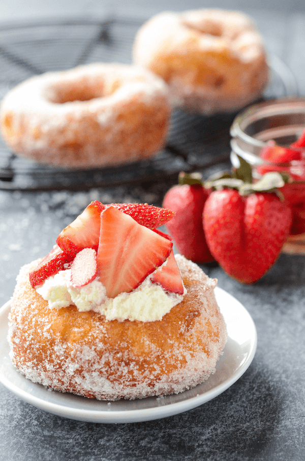 A Strawberry Shortcake Donut on a Plate with Fresh Strawberries and Two More Donuts in the Background