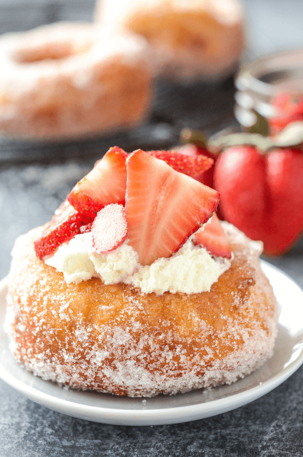 A Strawberry Shortcake Donut on a White Plate with Whipped Cream and Strawberry Slices on Top
