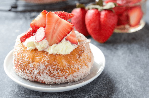A Homemade Donut on a Plate with Whipped Cream and Strawberry Slices on Top