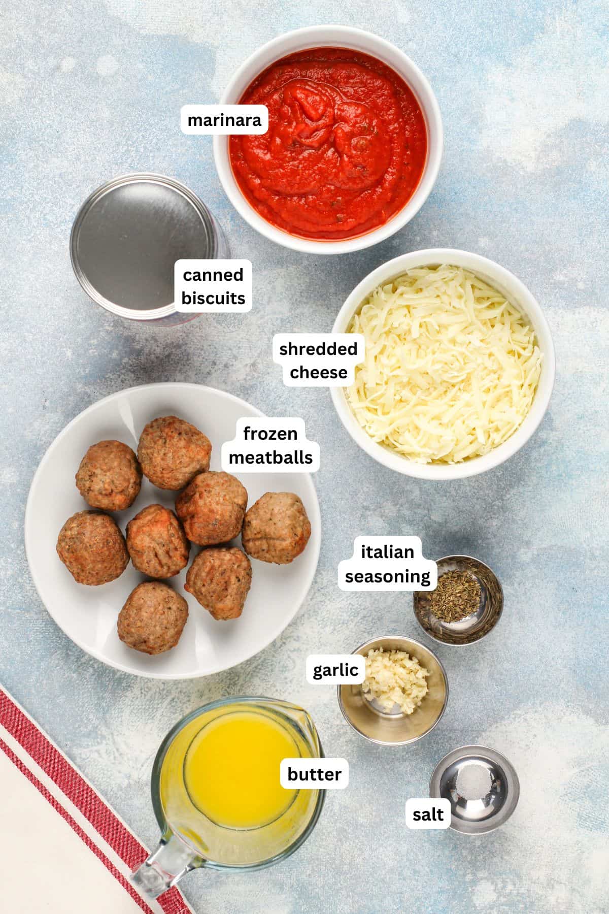 Ingredients for meatball bomb recipe in order from top to bottom: marinara, canned biscuits, shredded cheese, frozen meatballs, Italian seasoning, garlic, butter, salt.