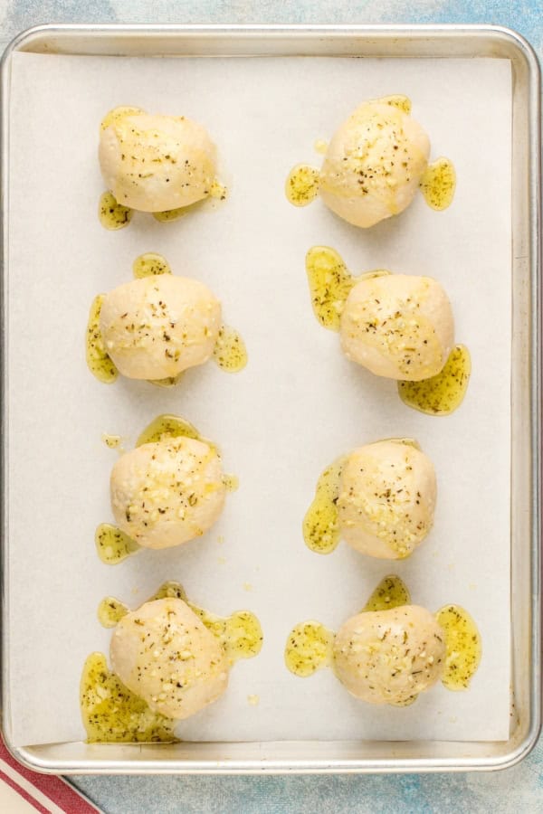 Uncooked meatball bombs are spread on a prepared baking sheet.