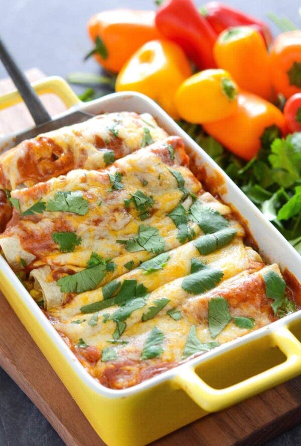 Enchiladas in casserole dish being scooped up with a spatula. 