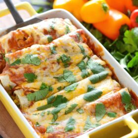 Enchiladas in casserole dish being scooped up with a spatula.