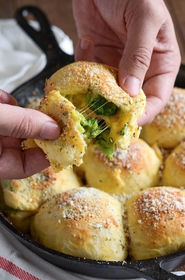 Hands pulling apart a biscuit stuffed with broccoli and cheese.