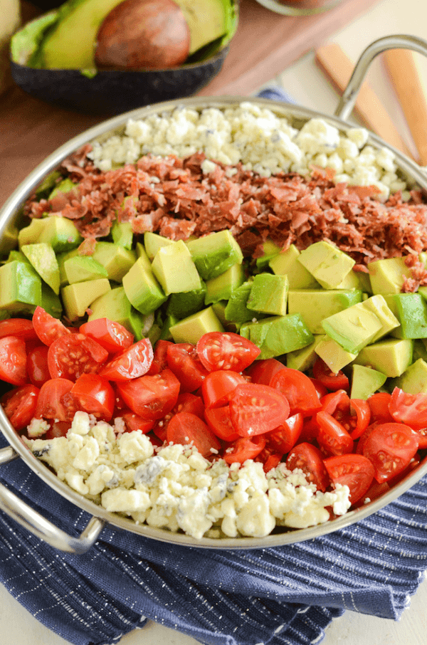 Copycat Maggianos Chopped Salad - blue cheese, tomatoes, avocados, bacon in a silver serving dish on a blue and white cloth