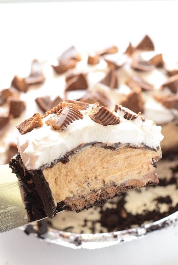 A slice of No-Bake Reese's Peanut Butter Pie with the rest of the pie in the background.