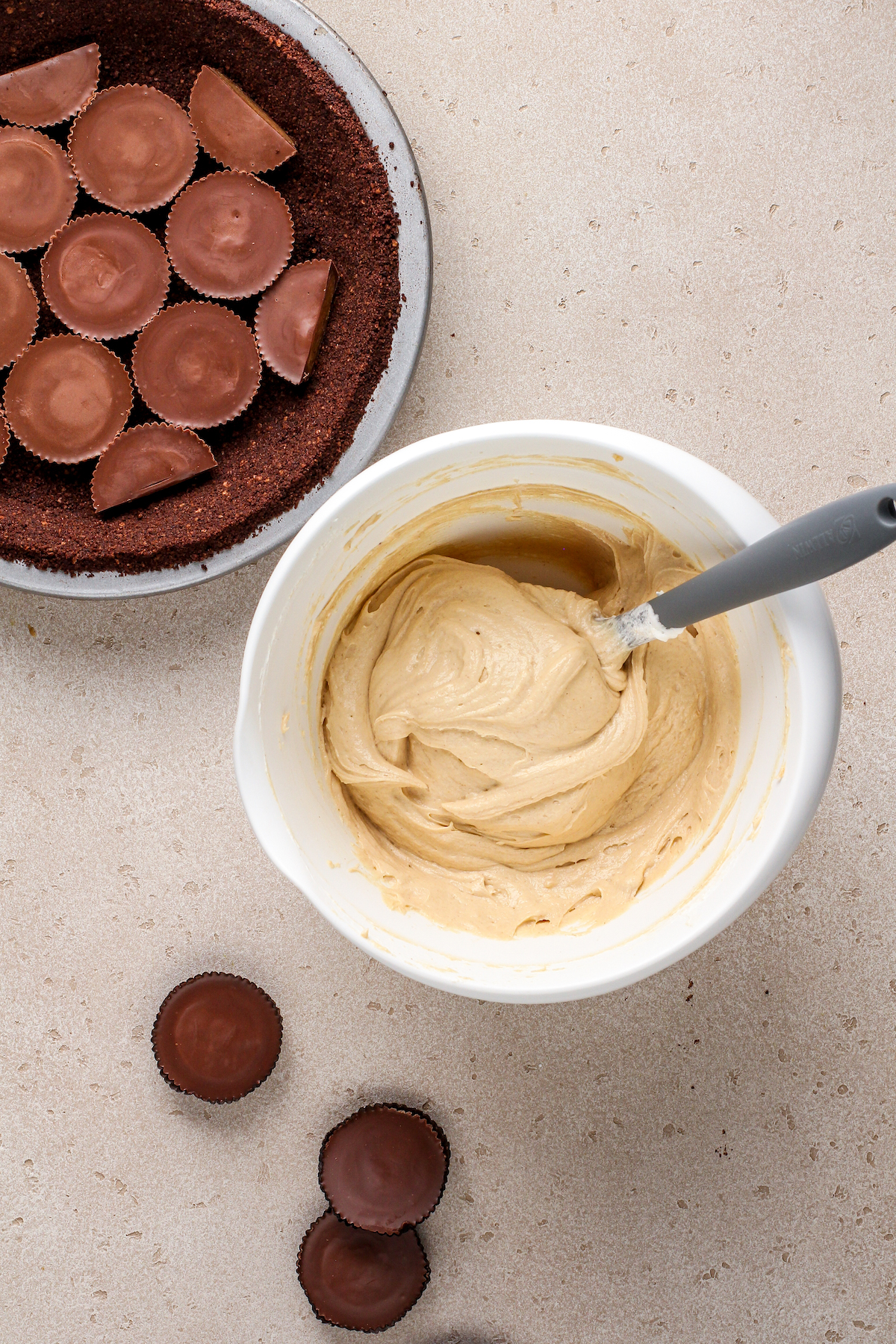 A bowl of creamy peanut butter filling next to a pie crust with peanut butter cups in it.