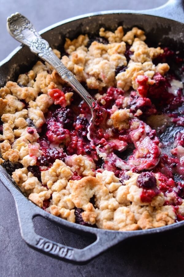 Skillet Berry Cobbler in a cast iron skillet topped with crumble - and a silver serving spoon. Much of the cobbler has been served.