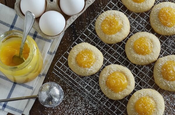 Lemon Thumbprint Cookies on a Cooling Rack Beside a Carton of Eggs, A Jar of Curd and a Sifter