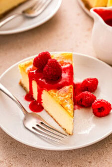 Slice of creme brulee cheesecake with fresh raspberries and fruity raspberry sauce on top.