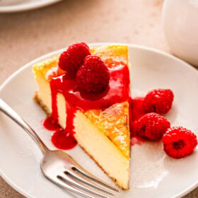 Slice of creme brulee cheesecake with fresh raspberries and fruity raspberry sauce on top.