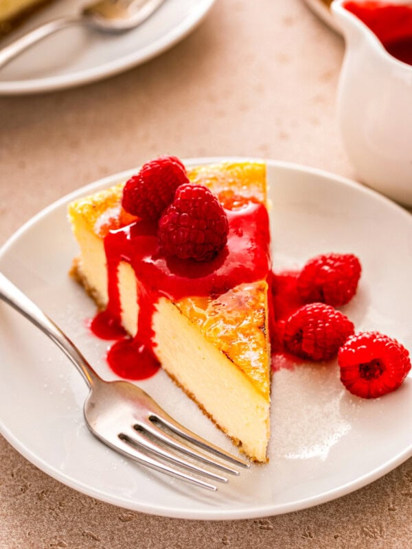 Slice of creme brulee cheesecake with fresh raspberries and fruity raspberry sauce on top.