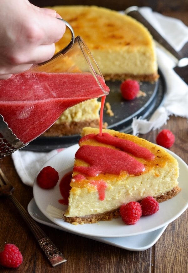 Raspberry Sauce being Poured Over a Slice of Cheesecake on a White Plate