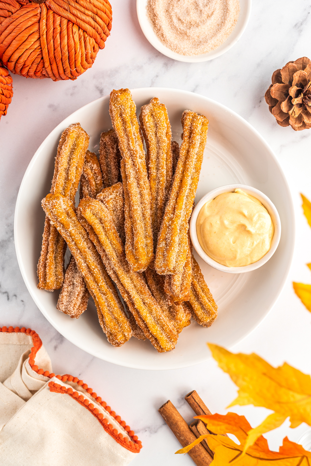 Pumpkin churros on a plate with cream cheese frosting on the side.