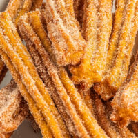Lots of pumpkin churros on a plate with cream cheese dip on the side.