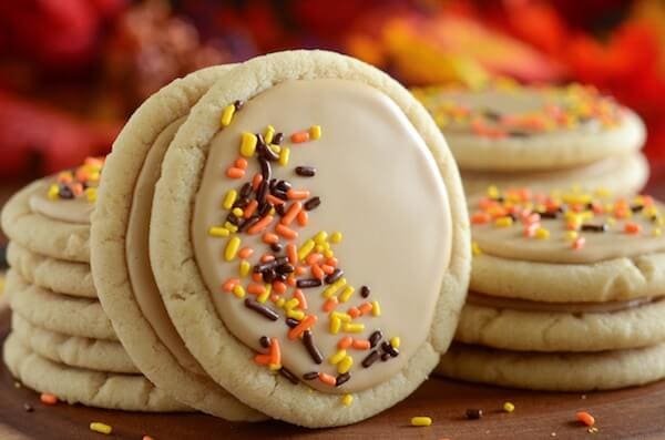 Stacks of soft maple sugar cookies with two frosted cookies with sprinkles in the foreground.