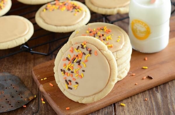 Soft maple sugar cookies frosted with maple icing and topped with orange and black sprinkles on a wooden board.